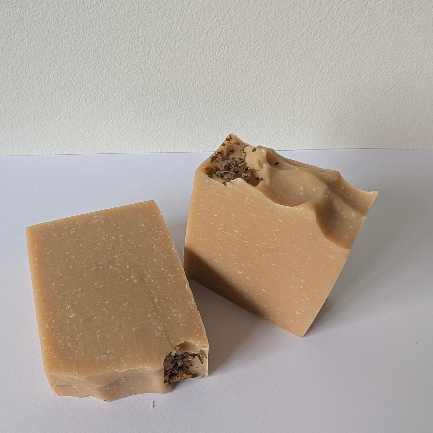 Two beige bars of soap on a white surface with a plain background