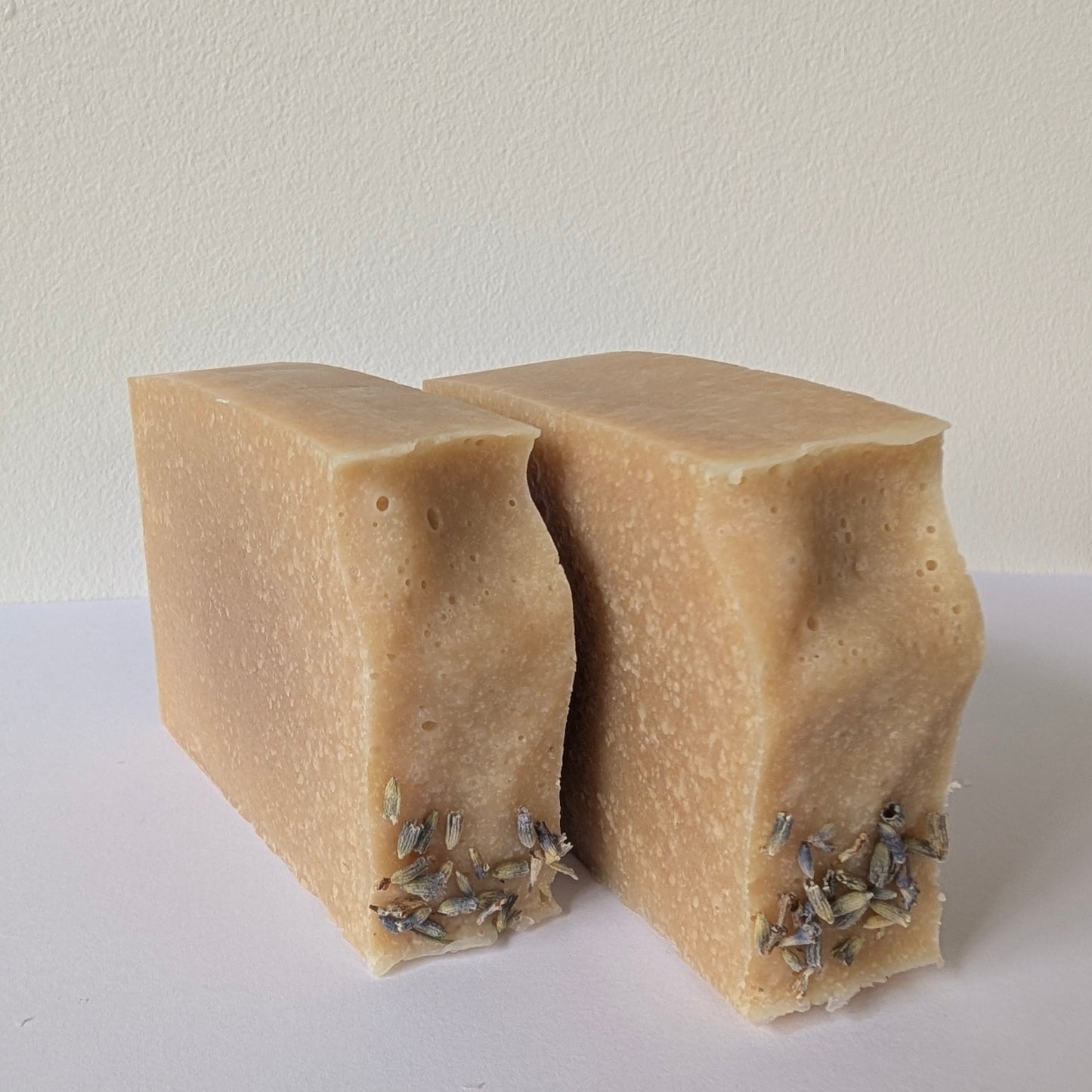 Two beige bars of soap with visible herbs on a white surface and background